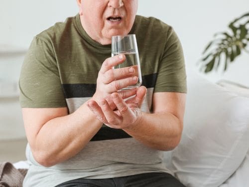 Il tremore è uno dei principali sintomi del Morbo di Parkinson: scopri come si blocca. Uomo cerca di tenersi la mano ferma per non tremare mentre beve un bicchiere d'acqua
