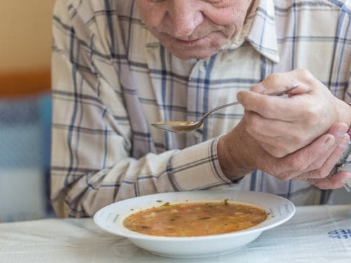 Scopri quali sono i sintomi principali del Morbo di Parkinson. Signore anziano si mantiene la mano per non tremare mentre mangia
